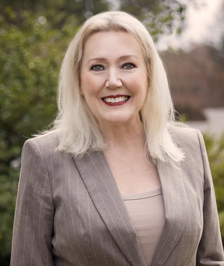 Beverly in a suit, standing outdoors with blurred background.