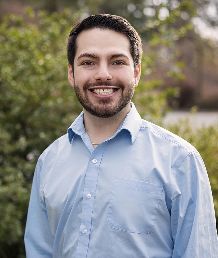 Ethan smiling outdoors with greenery in the background.