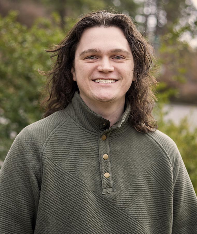 Mason in a green sweater smiling outdoors with trees in the background.