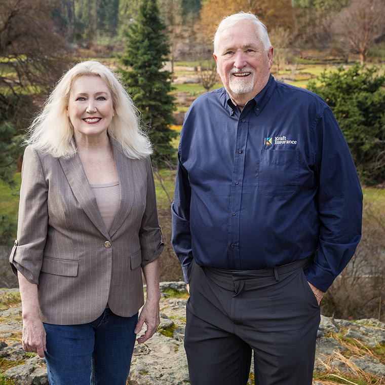 Two individuals smiling outdoors in a garden setting.