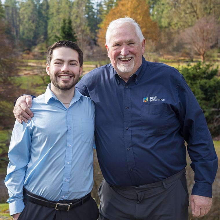 Two smiling people standing outdoors in a natural setting.