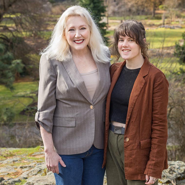 Two people standing outdoors, smiling in a sunny landscape.