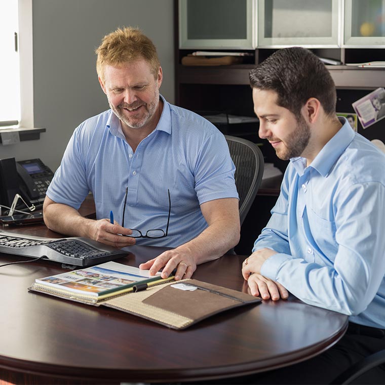 Two people in an office discussing documents at a desk.
