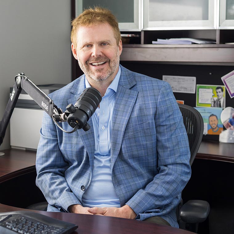 Person smiling at a desk with a microphone, in an office setting.
