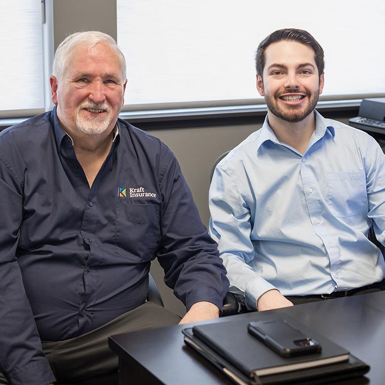 Two men smiling, seated at a desk with electronic devices.