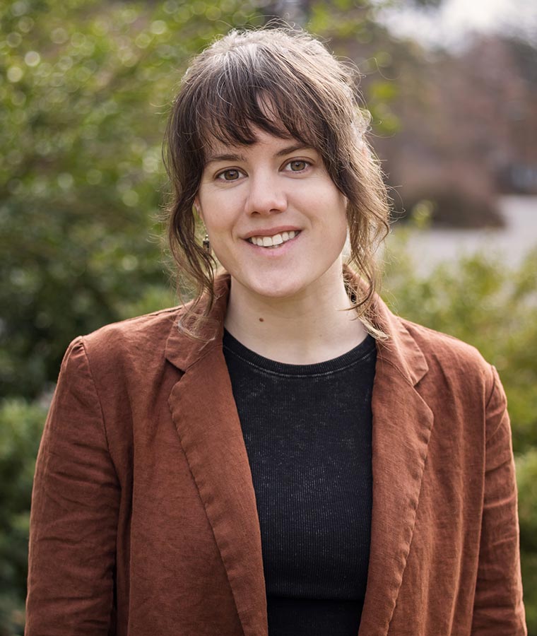 Nicole smiling outdoors with blurred greenery in the background.